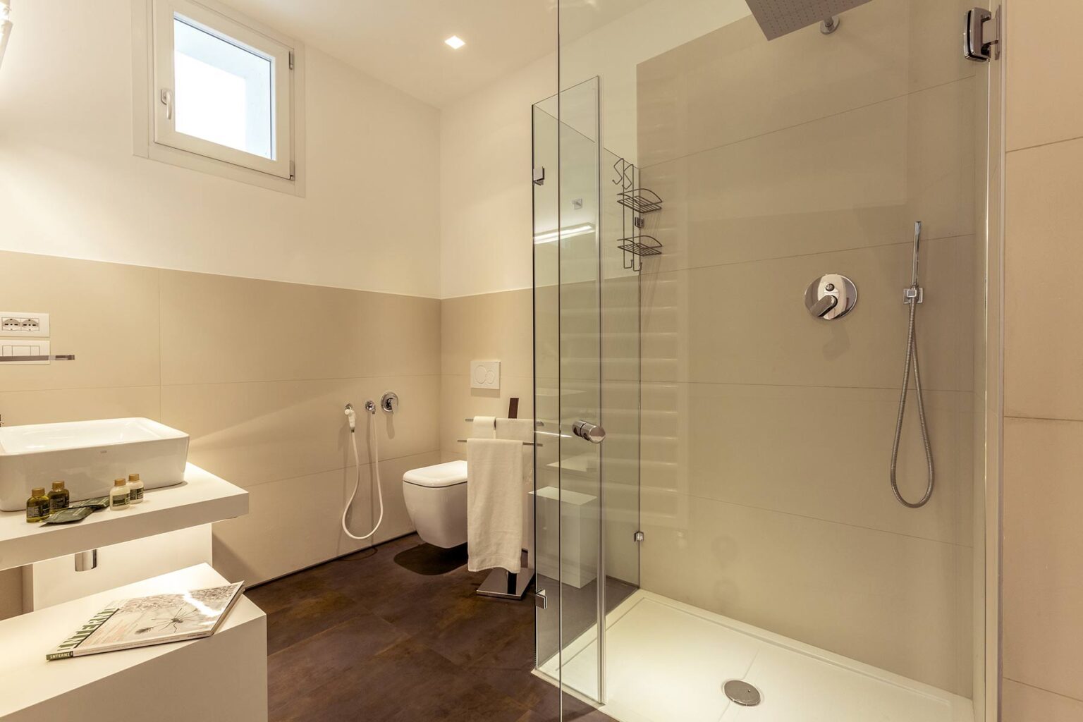 Modern bathroom featuring a glass shower enclosure, minimalist design, and neutral color palette. The space includes a sleek toilet, stylish sink, and natural light from a window, creating a clean and inviting atmosphere. | Only on SopranoVillas