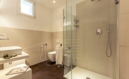 Modern bathroom featuring a glass shower enclosure, minimalist design, and neutral color palette. The space includes a sleek toilet, stylish sink, and natural light from a window, creating a clean and inviting atmosphere.
