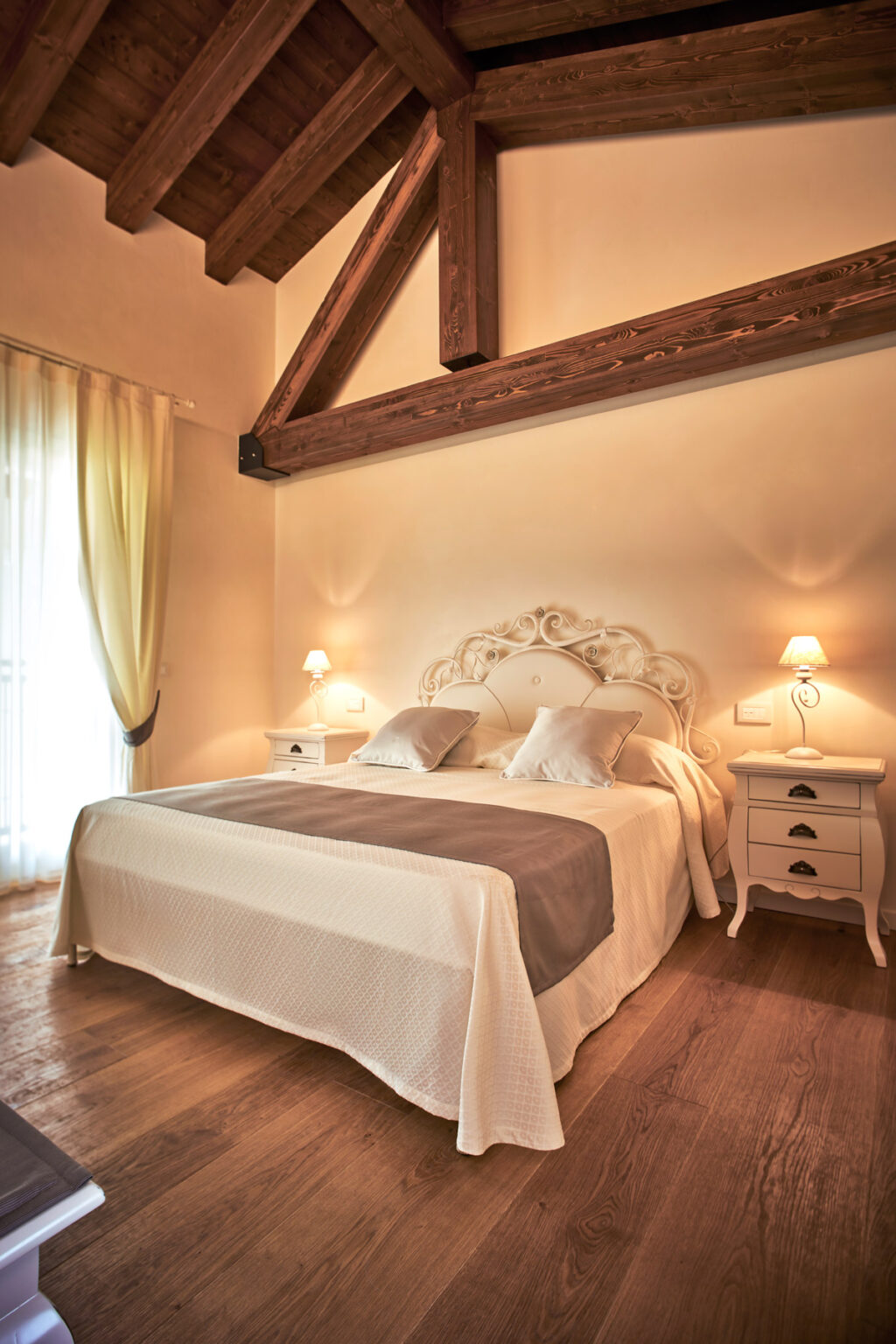 Elegant bedroom featuring a cozy double bed with decorative pillows, wooden beams on the ceiling, and soft lighting. The room includes stylish nightstands and sheer curtains, creating a warm and inviting atmosphere. Ideal for relaxation and comfort. | Only on SopranoVillas