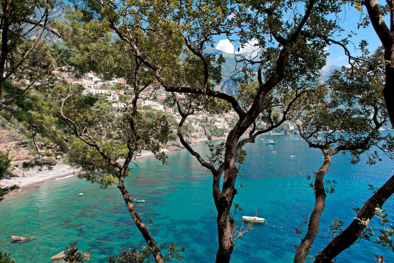 Scenic view of a coastal landscape featuring turquoise waters, rocky shoreline, and lush green trees, highlighting the natural beauty of a Mediterranean destination. | Only on SopranoVillas