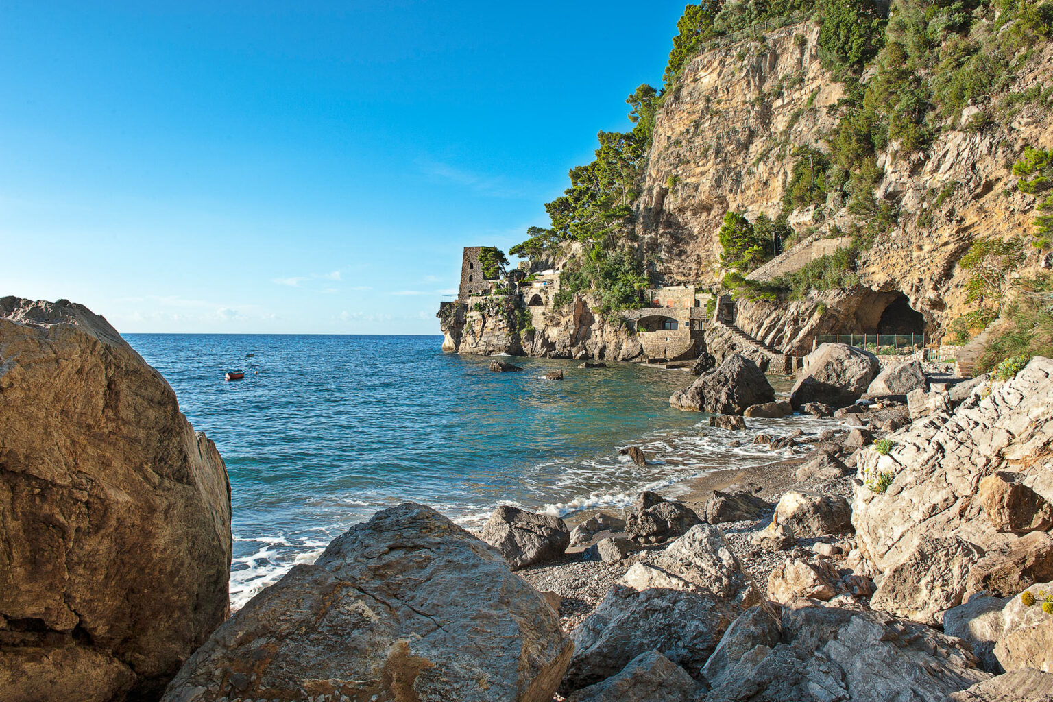 Scenic coastal view featuring rocky shoreline, clear blue water, and lush greenery on cliffs, ideal for nature lovers and outdoor enthusiasts. | Only on SopranoVillas
