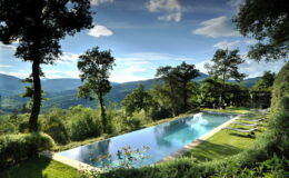 Scenic view of a modern infinity pool surrounded by lush greenery and hills under a clear blue sky, ideal for luxury vacation rentals or serene retreats.