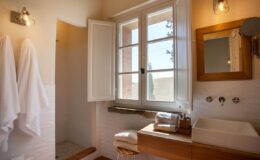 Bright and modern bathroom featuring large windows, wooden accents, a stylish sink, and neatly hung white towels. Natural light enhances the spacious feel of the room.