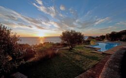 Scenic view of a sunset over the ocean, featuring a lush garden with trees and a swimming pool, creating a tranquil atmosphere.