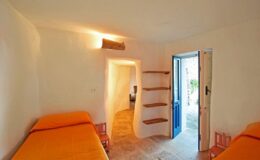 Cozy interior of a minimalist room featuring two orange beds, a small bookshelf, and a door leading outside, designed for relaxation and comfort.