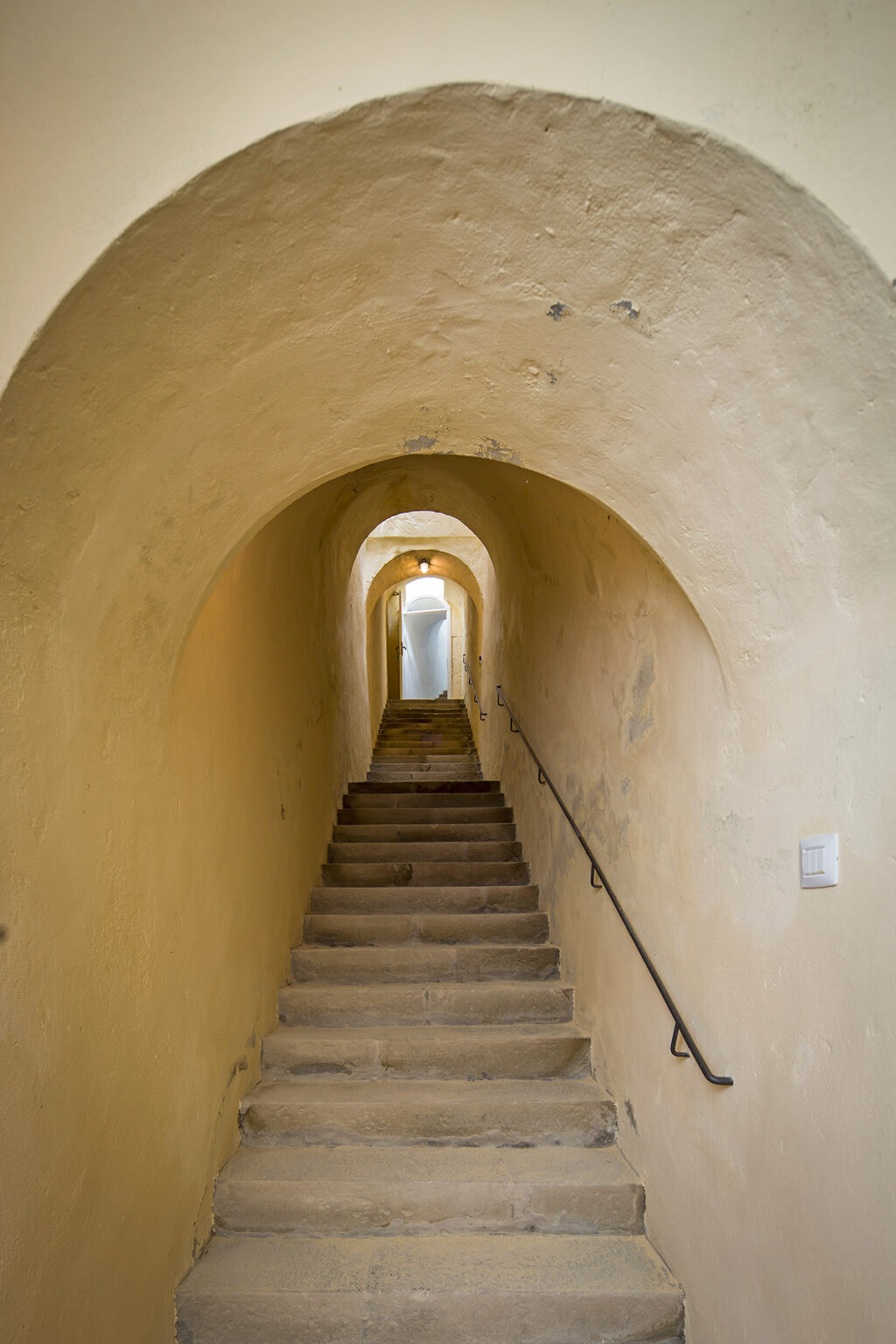 Narrow stone staircase leading through an arched hallway with warm yellow walls, illuminated by soft lighting, creating an inviting atmosphere. | Only on SopranoVillas