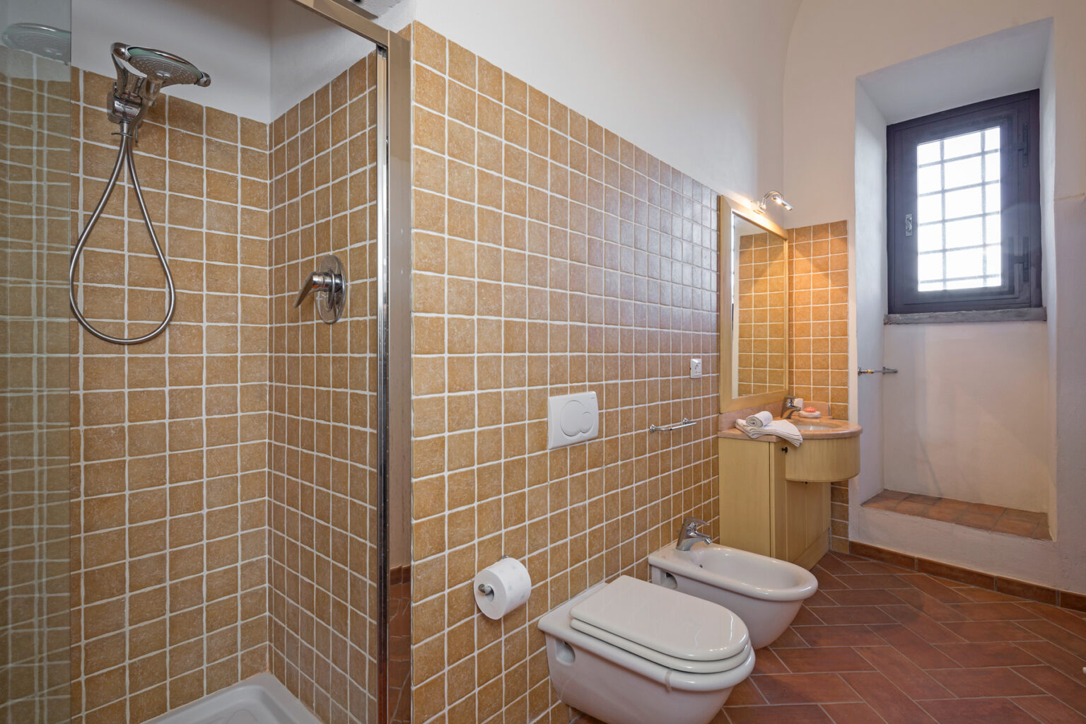 Modern bathroom featuring a walk-in shower, beige tiled walls, a toilet, and a sink with a mirror. Natural light enters through a window, creating a bright and inviting atmosphere. | Only on SopranoVillas