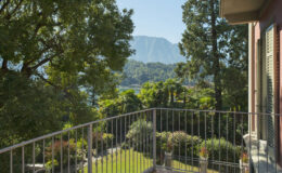 Scenic view from a balcony overlooking lush greenery and mountains, with a clear blue sky and vibrant foliage in the foreground. Ideal for showcasing serene outdoor living spaces and natural landscapes.