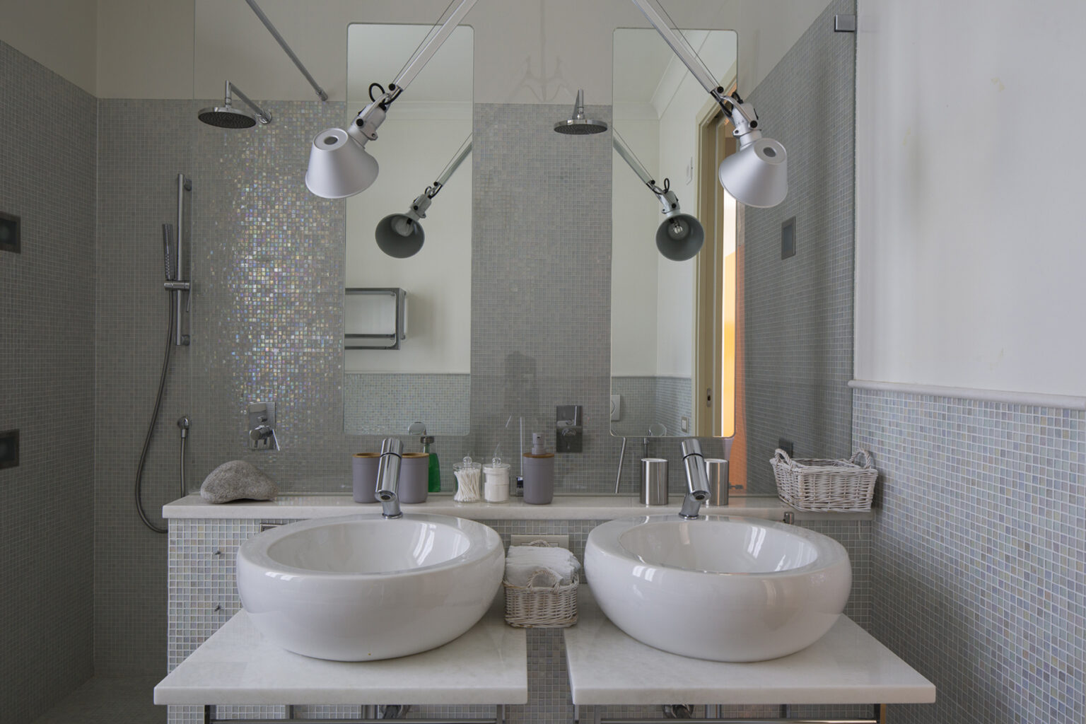 Modern bathroom design featuring a double vanity with two white vessel sinks, stylish wall-mounted faucets, and contemporary lighting. The space includes a walk-in shower with sleek fixtures and a minimalist aesthetic, complemented by mosaic tiles and a bright, airy feel. | Only on SopranoVillas