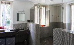 Modern bathroom interior featuring a glass shower enclosure, sleek dark cabinetry, and natural light streaming through large windows. The walls are adorned with stylish gray tiles, creating an elegant and spacious atmosphere.