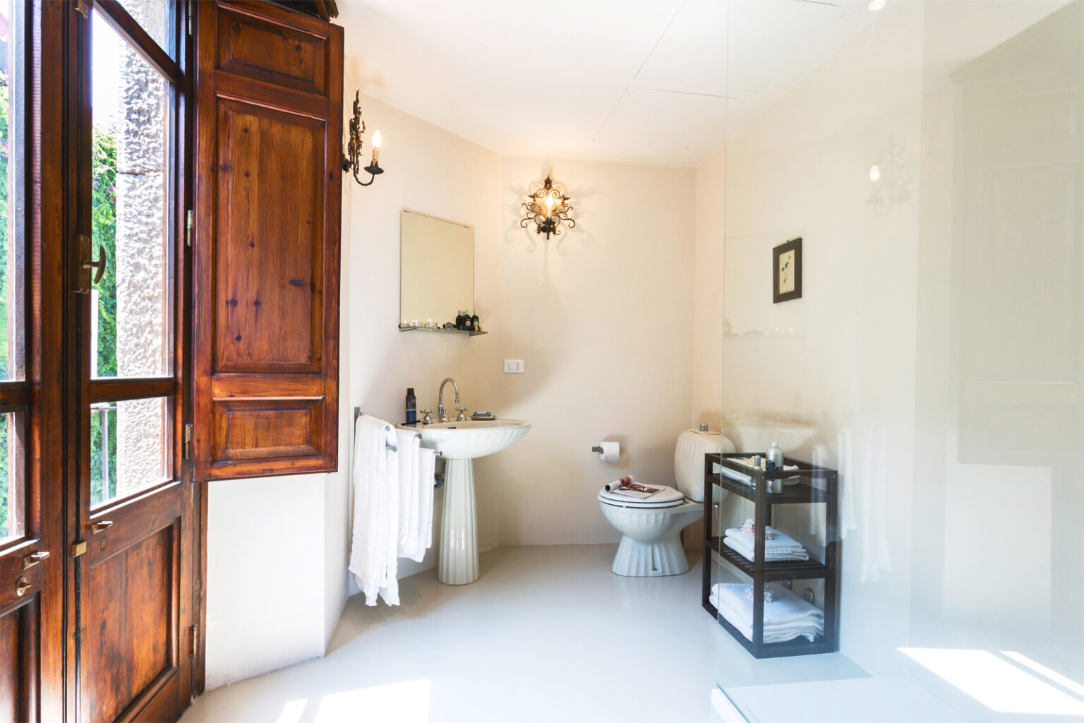 Bright and airy bathroom featuring a wooden window, a modern sink, a toilet, and a stylish storage cart. Natural light illuminates the space, highlighting the minimalist design and elegant decor elements. | Only on SopranoVillas