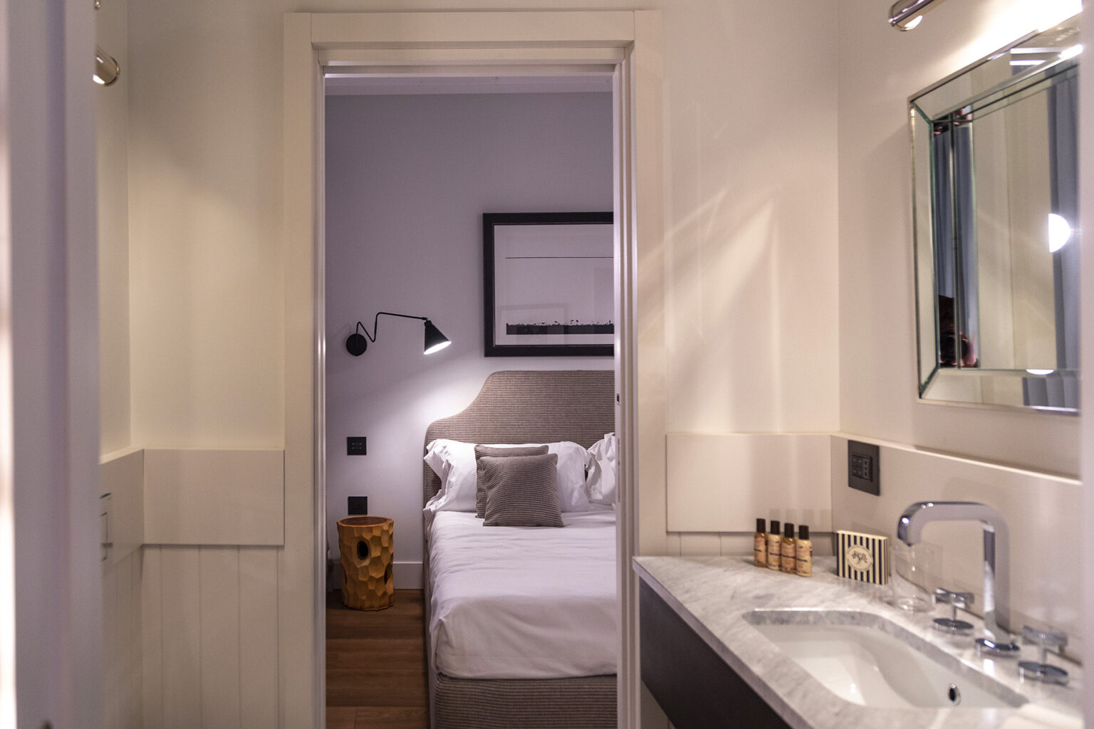 Interior view of a modern hotel room featuring a cozy bed, stylish decor, and a well-equipped bathroom with a sleek sink and mirror. The design emphasizes comfort and elegance, ideal for travelers seeking a relaxing stay. | Only on SopranoVillas