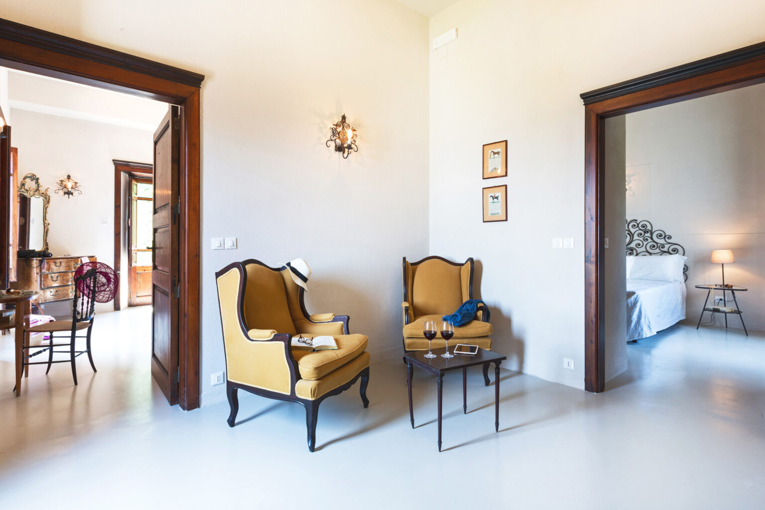 Cozy living area featuring two yellow armchairs and a small table, with a view into a well-lit bedroom and dining area, highlighting a warm and inviting interior design. | Only on SopranoVillas