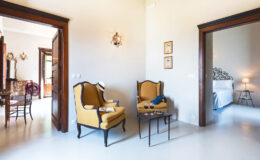 Cozy living area featuring two yellow armchairs and a small table, with a view into a well-lit bedroom and dining area, highlighting a warm and inviting interior design.
