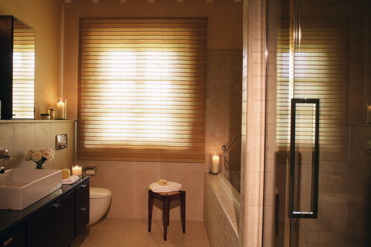 Modern bathroom interior featuring a sleek shower, elegant vanity with sink, and natural light filtering through bamboo window shades. The space is accented with candles and a small stool, creating a serene atmosphere. | Only on SopranoVillas