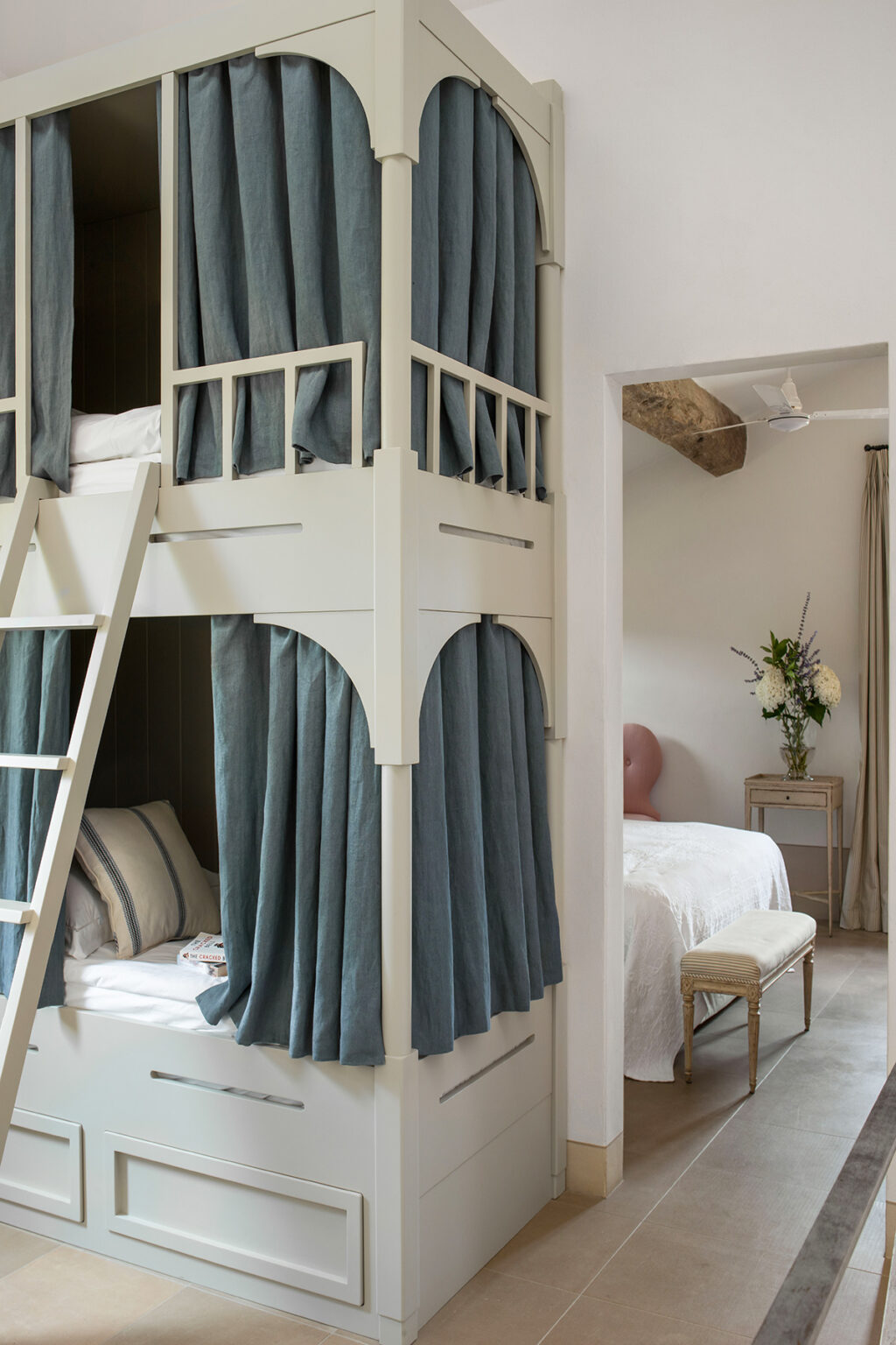Cozy children's bedroom featuring a stylish loft bed with a ladder and soft blue curtains, complemented by a serene white bed and decorative flowers in a vase. | Only on SopranoVillas
