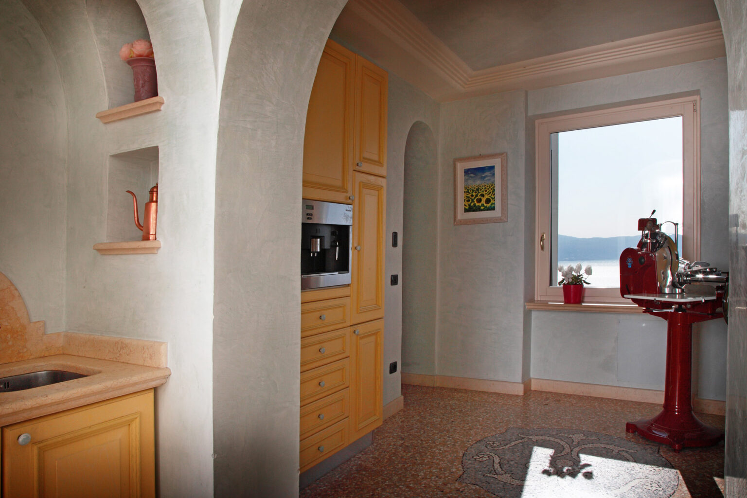 Bright and airy kitchen featuring yellow cabinetry, modern appliances, and a scenic view of the outdoors through a large window. The design includes archways and decorative elements, creating a warm and inviting atmosphere. | Only on SopranoVillas