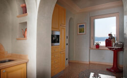 Bright and airy kitchen featuring yellow cabinetry, modern appliances, and a scenic view of the outdoors through a large window. The design includes archways and decorative elements, creating a warm and inviting atmosphere.