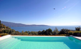 Scenic view of a tranquil swimming pool overlooking a serene lake and distant mountains under a clear blue sky.