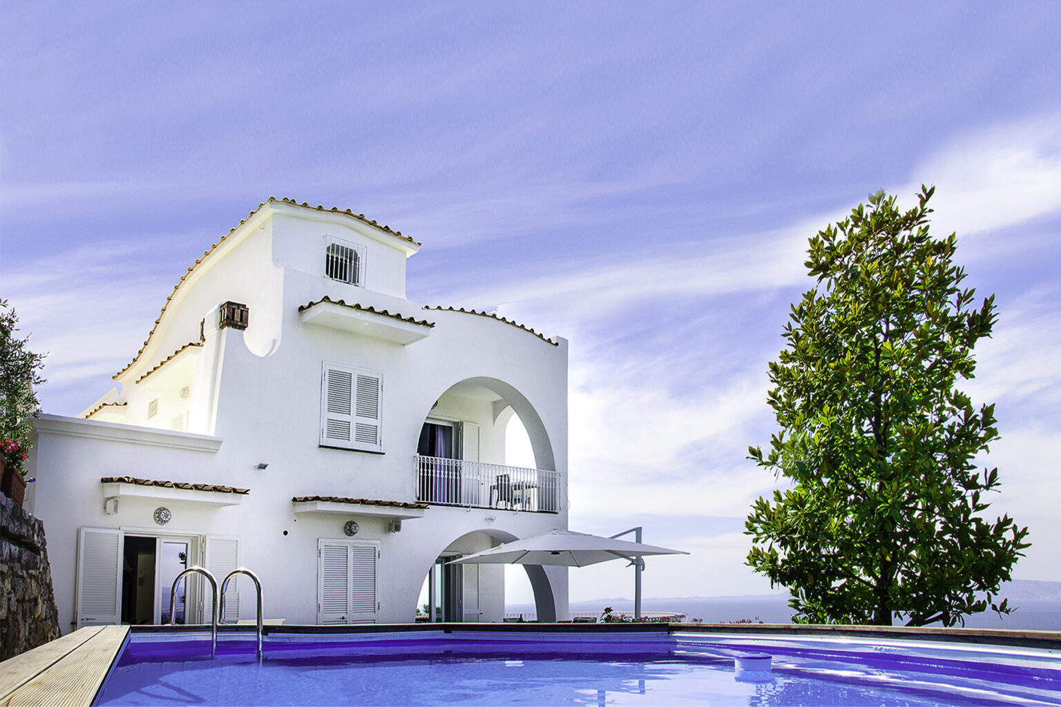 Modern white villa with a swimming pool, surrounded by lush greenery and a clear blue sky, ideal for luxury getaways. | Only on SopranoVillas
