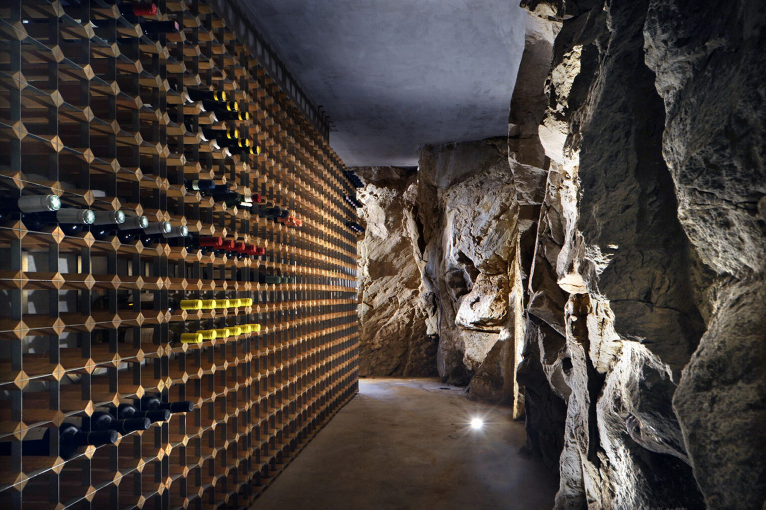 Wine cellar featuring a modern design with a wooden wine rack against a natural rock wall, illuminated by soft lighting, creating an elegant and inviting atmosphere for wine storage. | Only on SopranoVillas