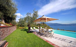 Beautiful outdoor pool area with sun loungers and an umbrella, overlooking a serene lake and lush greenery, ideal for relaxation and leisure activities.