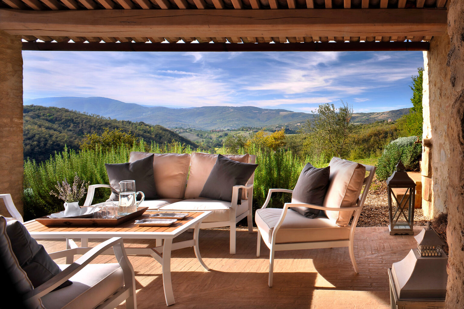 Cozy outdoor seating area with plush cushions overlooking a scenic mountain landscape, surrounded by greenery and bright blue skies, perfect for relaxation and enjoying nature. | Only on SopranoVillas