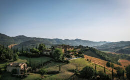 Scenic view of a rustic villa in the Tuscan countryside, surrounded by rolling hills and vineyards under a clear blue sky. Ideal for travel enthusiasts and nature lovers.