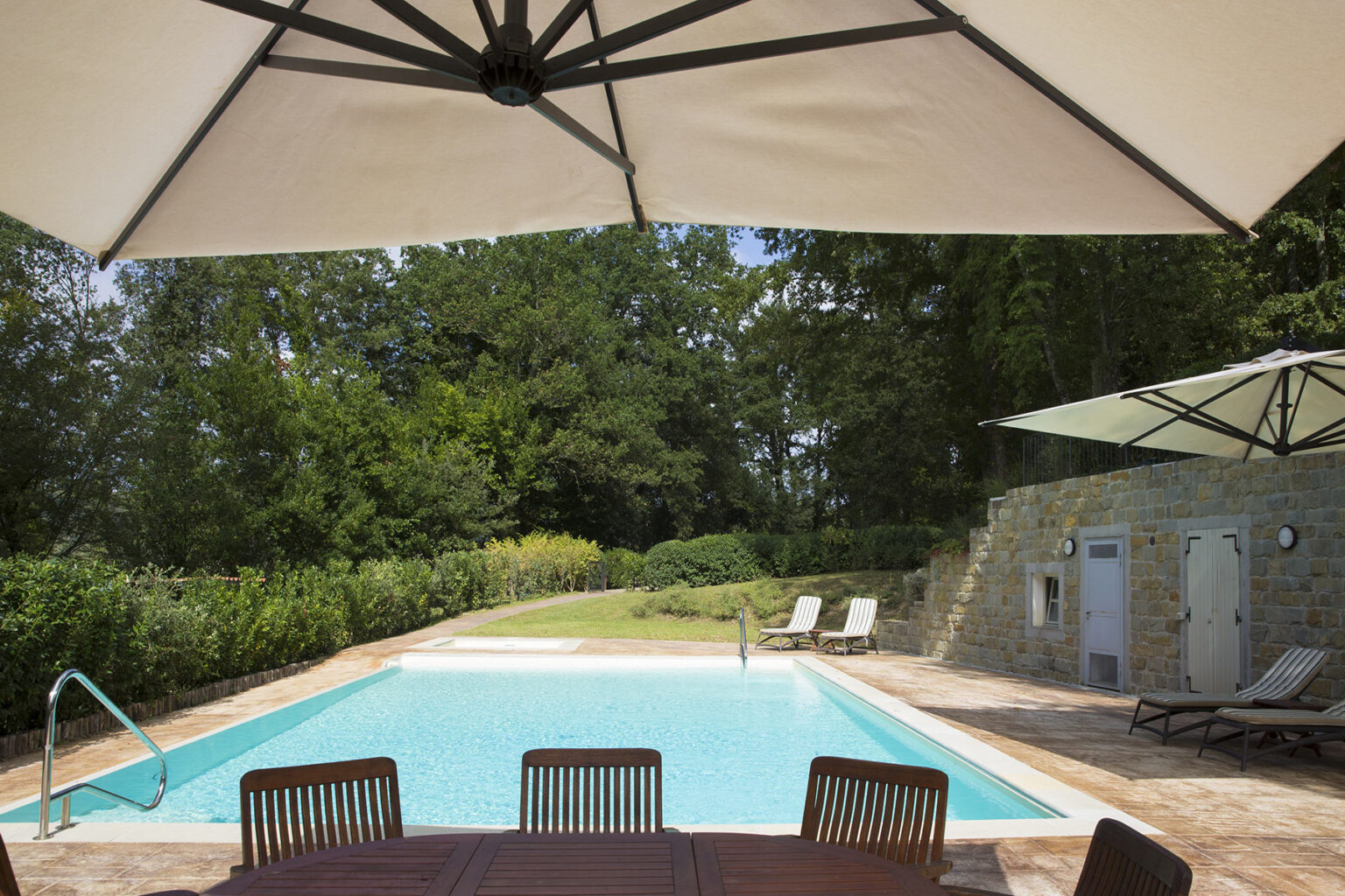 Outdoor swimming pool surrounded by greenery, featuring lounge chairs and a large umbrella for shade, ideal for relaxation and leisure. | Only on SopranoVillas