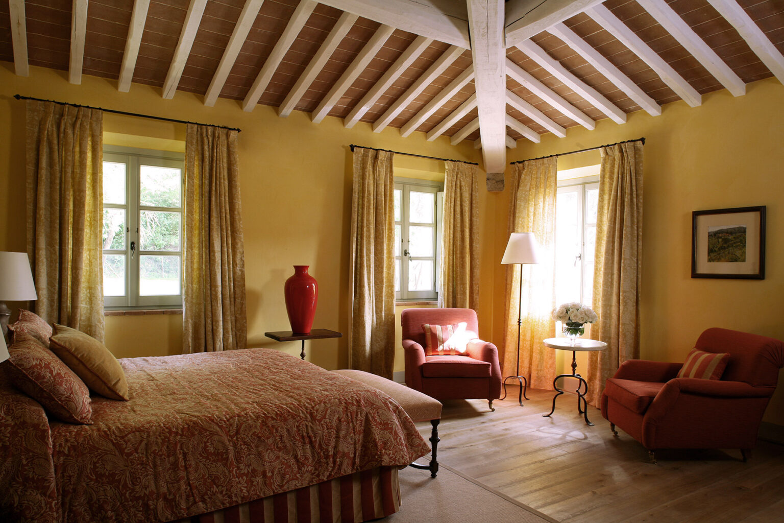 Cozy bedroom featuring a queen-sized bed with decorative bedding, two comfortable armchairs, large windows with yellow curtains, and a wooden ceiling with exposed beams, creating a warm and inviting atmosphere. | Only on SopranoVillas