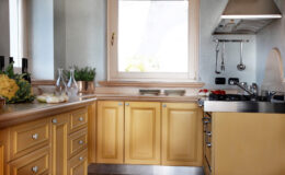Modern kitchen featuring yellow cabinetry, a stainless steel countertop, and a window that brightens the space. The kitchen is equipped with a gas stove and hanging utensils, creating a functional and inviting cooking environment.