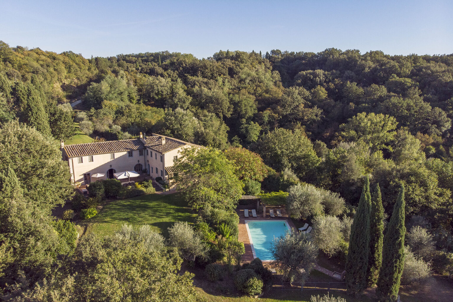 Aerial view of a rustic villa surrounded by lush greenery, featuring a sparkling swimming pool and landscaped gardens, ideal for a tranquil getaway. | Only on SopranoVillas