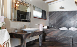 Modern bathroom featuring a sleek stone sink, large mirror, elegant lighting, and a stylish bathtub with plush towels, designed for a luxurious and relaxing atmosphere.