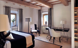 Modern bedroom interior featuring wooden beams, stylish furniture, and elegant decor. The room includes a black and white color scheme, a desk with a lamp, and large windows with drapes, creating a bright and inviting atmosphere.