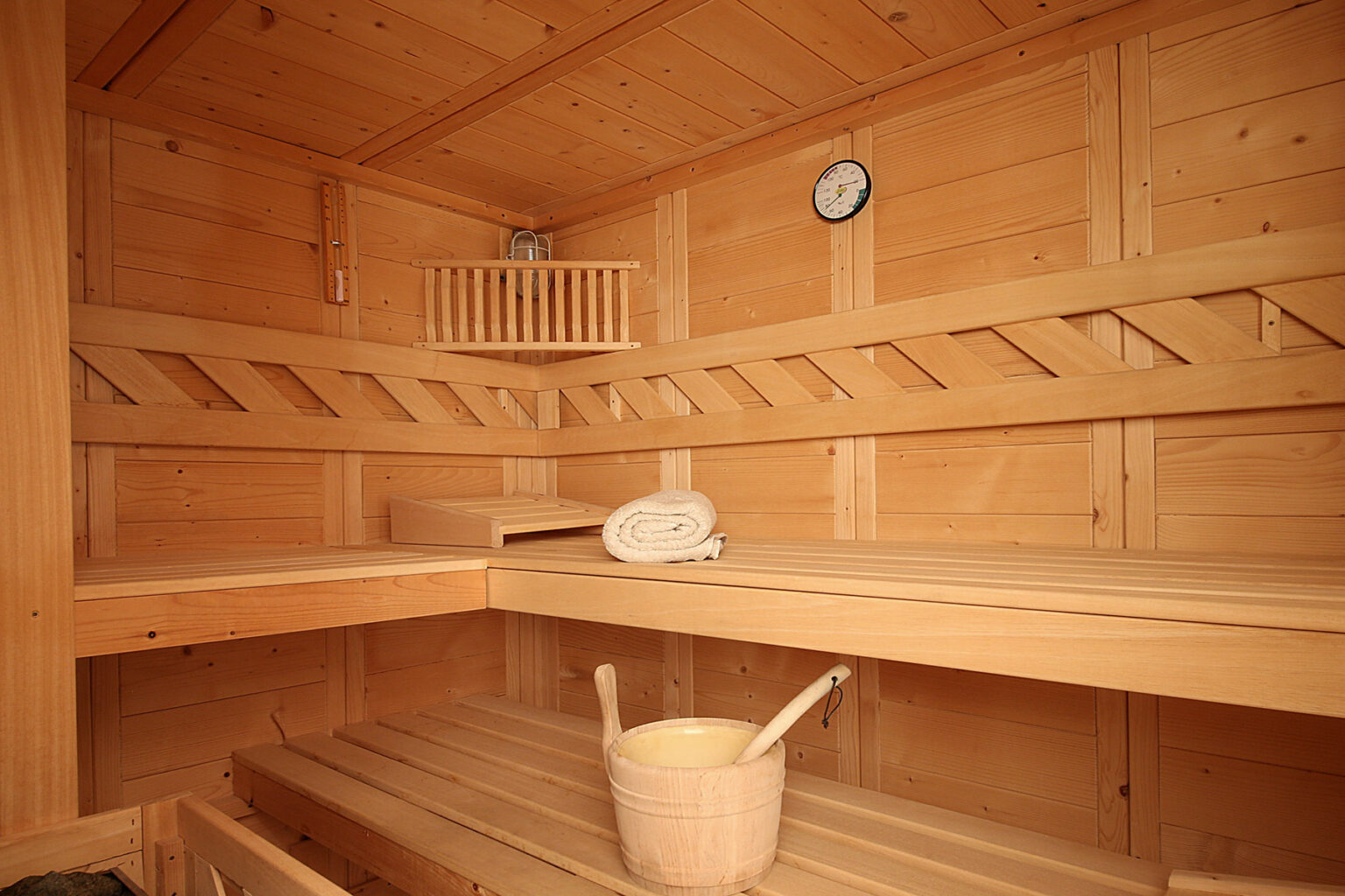Interior of a wooden sauna featuring two benches, a thermometer, a towel, and a wooden bucket, showcasing a relaxing wellness environment. | Only on SopranoVillas