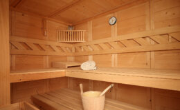 Interior of a wooden sauna featuring two benches, a thermometer, a towel, and a wooden bucket, showcasing a relaxing wellness environment.