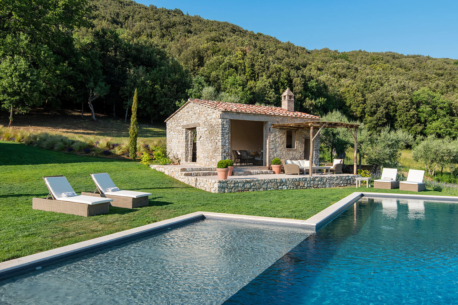 Stone villa with a pool surrounded by lush greenery, featuring sun loungers and a scenic hillside backdrop. Perfect for a relaxing getaway in nature. | Only on SopranoVillas