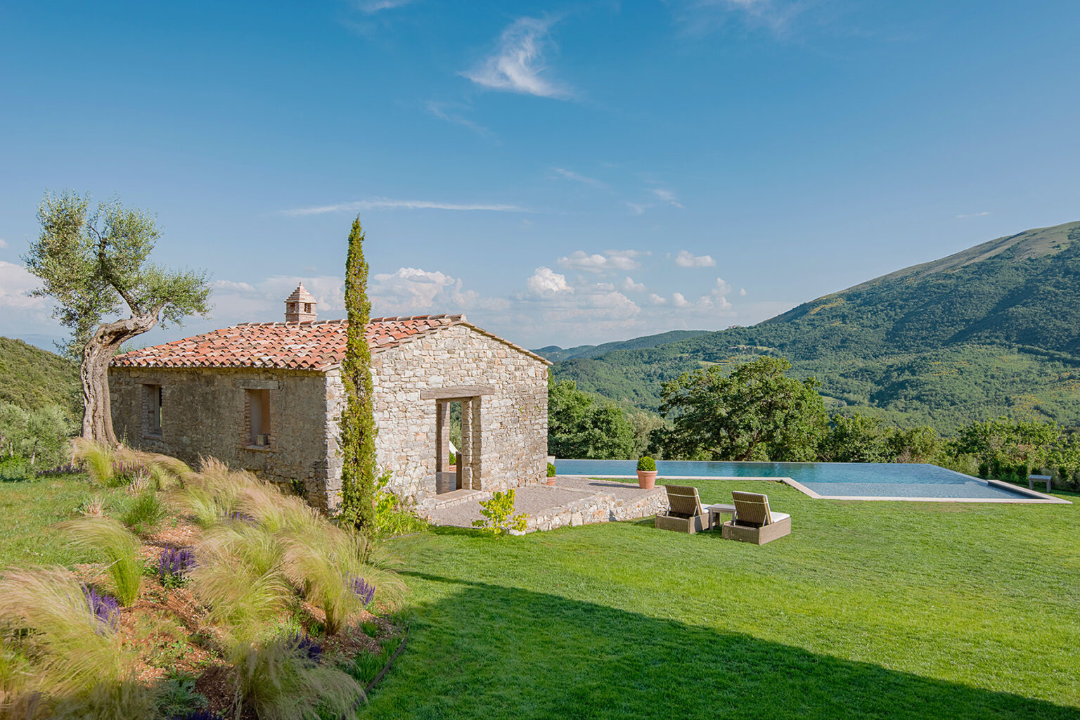 Rustic stone villa with a swimming pool set in a lush green landscape, surrounded by rolling hills and clear blue skies. Perfect for a relaxing getaway in nature. | Only on SopranoVillas