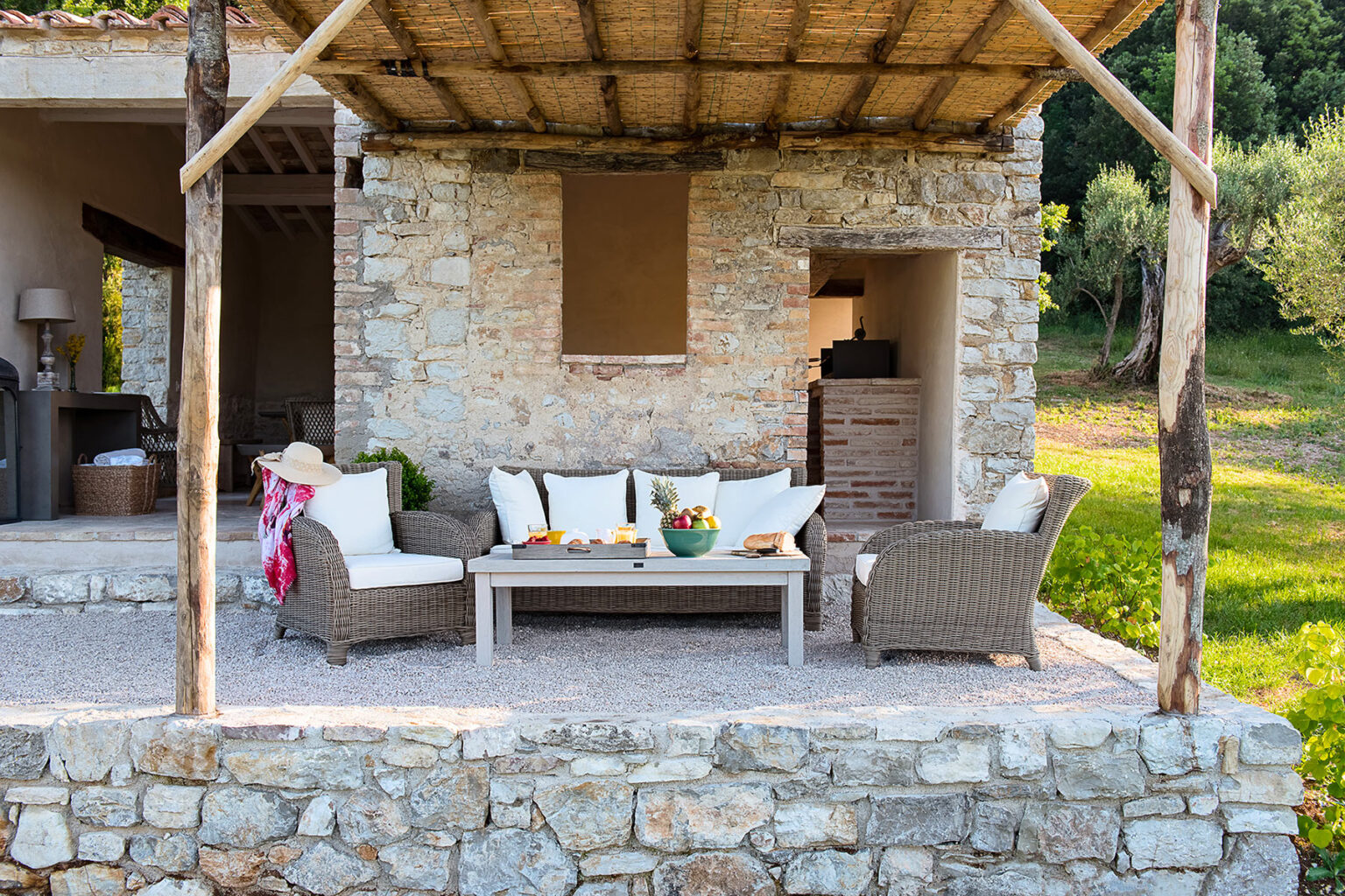 Cozy outdoor seating area with wicker furniture and decorative cushions, surrounded by lush greenery and a rustic stone wall, ideal for relaxation and entertaining. | Only on SopranoVillas