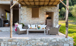 Cozy outdoor seating area with wicker furniture and decorative cushions, surrounded by lush greenery and a rustic stone wall, ideal for relaxation and entertaining.