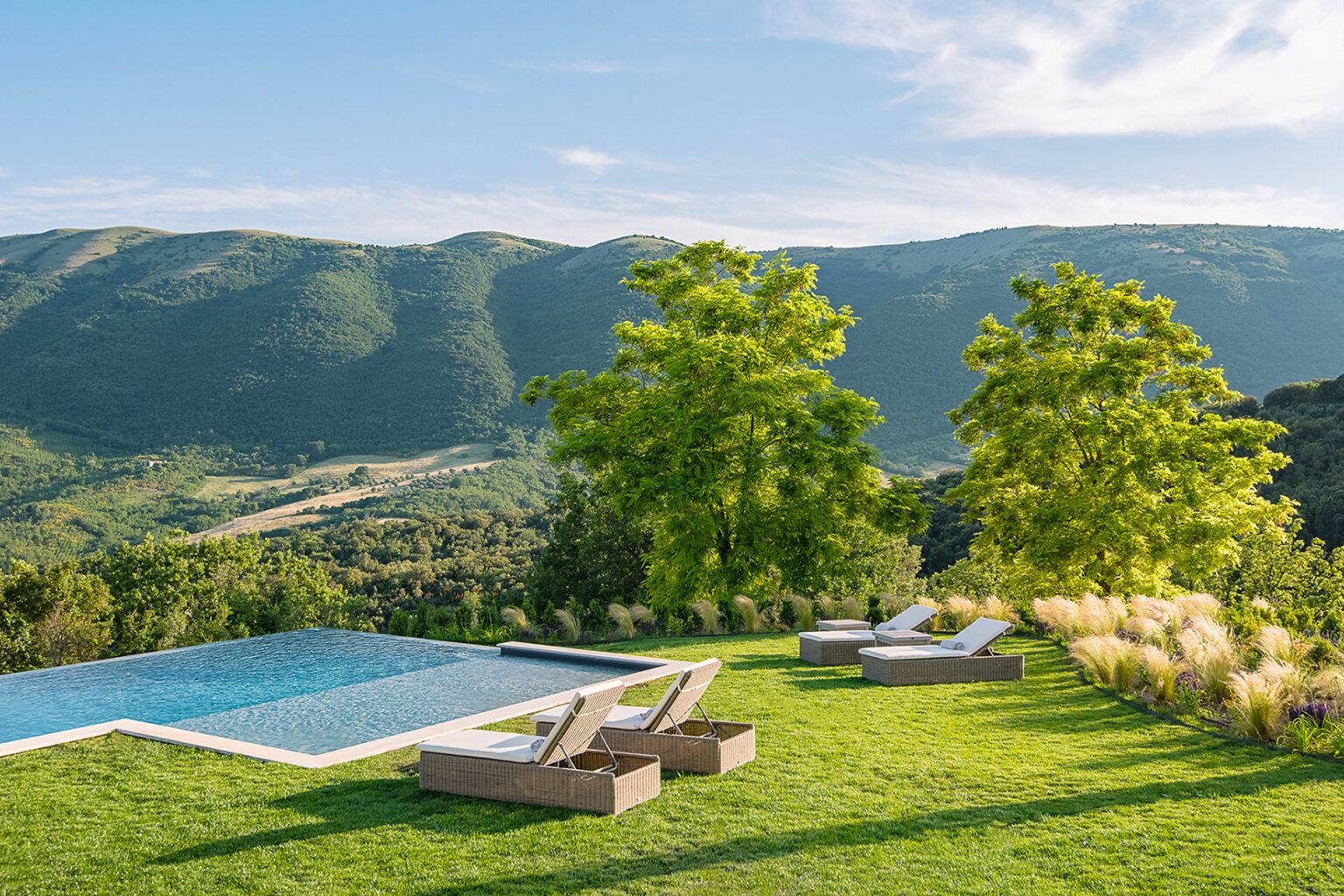 Modern outdoor living space featuring a luxurious infinity pool, lounge chairs, and lush greenery, with stunning mountain views in the background. Perfect for relaxation and entertainment. | Only on SopranoVillas