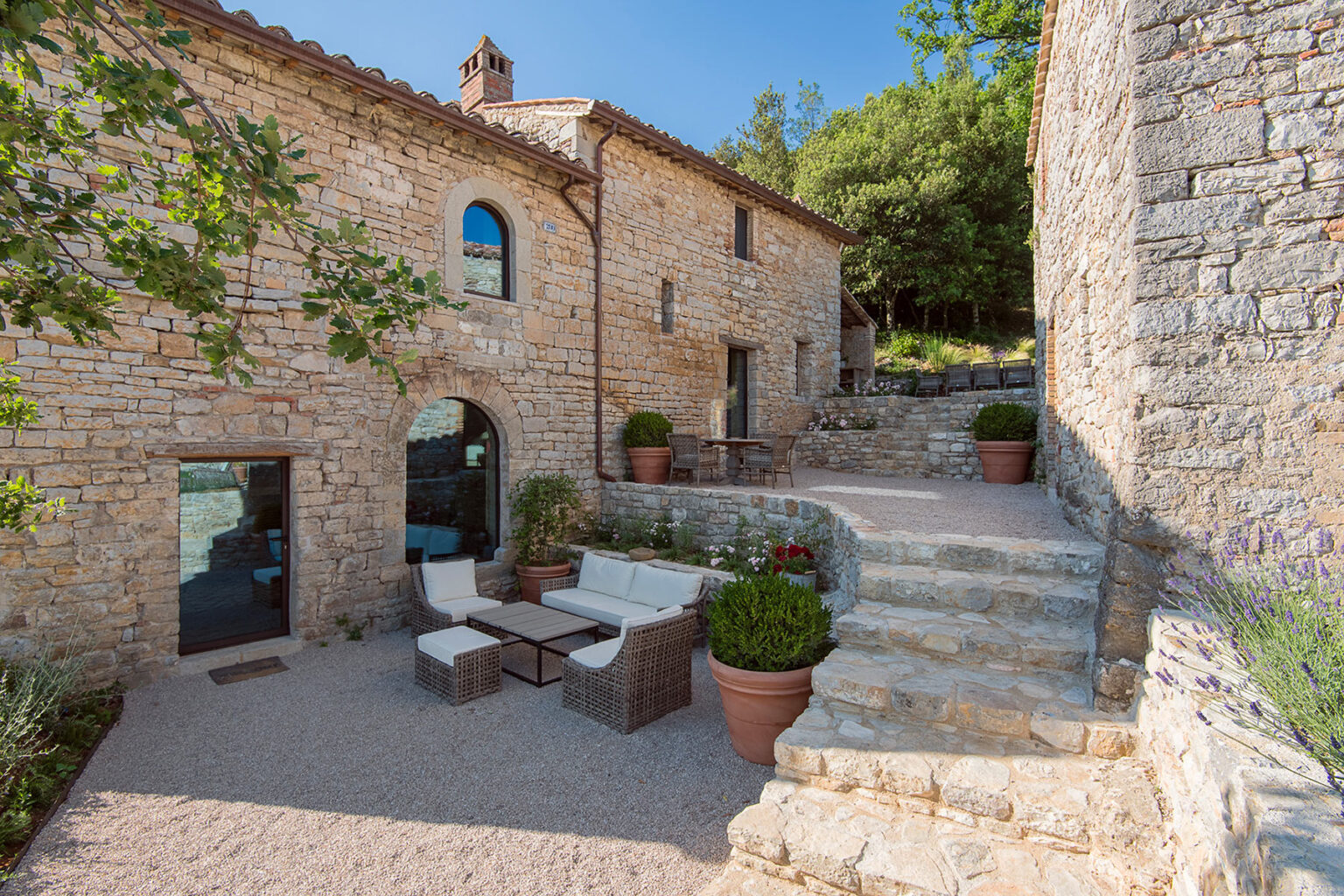 Charming stone cottage with outdoor seating area surrounded by greenery, featuring a staircase leading up to a scenic view. Ideal for relaxation and enjoying the natural surroundings. | Only on SopranoVillas