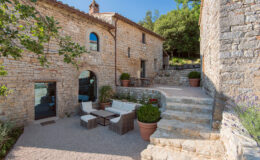 Charming stone cottage with outdoor seating area surrounded by greenery, featuring a staircase leading up to a scenic view. Ideal for relaxation and enjoying the natural surroundings.