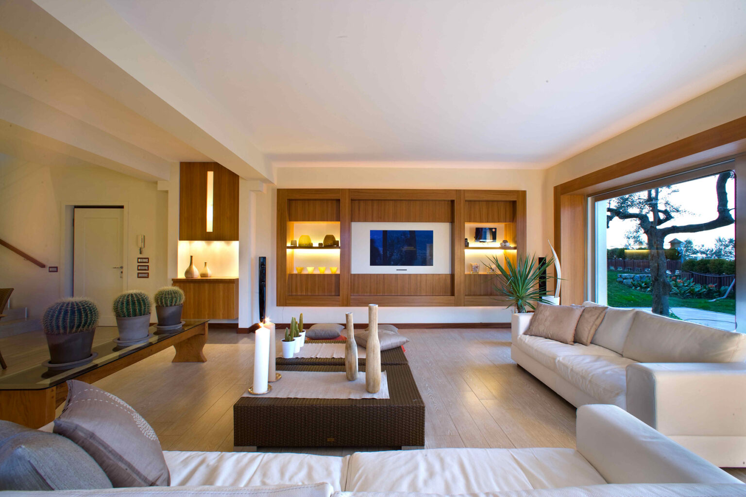 Modern living room featuring a spacious layout with large windows, natural light, contemporary furniture, and a stylish entertainment center. The design includes neutral tones, wooden accents, and decorative plants, creating a warm and inviting atmosphere. | Only on SopranoVillas