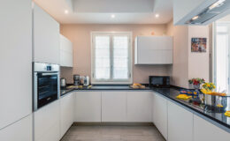 Modern kitchen design featuring sleek white cabinetry, a dark countertop, built-in oven, and ample natural light from a window. Stylish appliances and decorative elements enhance the contemporary aesthetic.