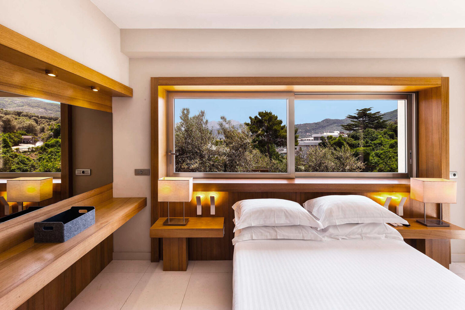 Modern bedroom with wooden accents, featuring a large window overlooking a scenic view. The room includes a neatly made bed, bedside lamps, and a stylish vanity area. | Only on SopranoVillas