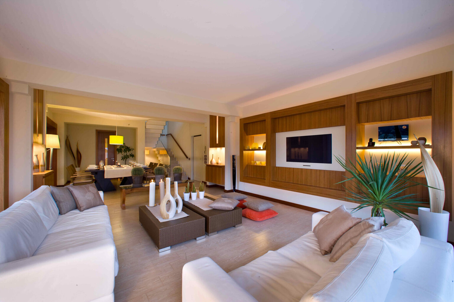 Modern living room with stylish white sofas, wooden accent walls, and a flat-screen TV. The space features a cozy coffee table, decorative vases, and indoor plants, creating a warm and inviting atmosphere. | Only on SopranoVillas