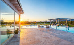 Modern luxury villa with a stunning swimming pool at sunset, featuring lounge chairs and a serene landscape in the background.