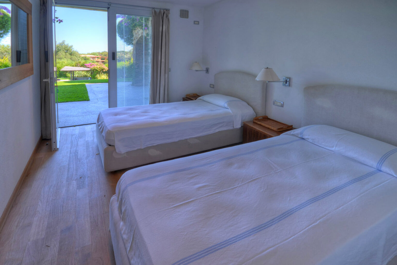 Bright and airy bedroom featuring two twin beds, wooden flooring, and large sliding glass doors leading to a garden view. Ideal for comfortable stays in a serene environment. | Only on SopranoVillas