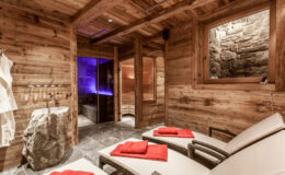 Relaxing wooden spa interior with lounge chairs, red towels, and a stone accent wall, featuring a sauna and ambient lighting for a tranquil atmosphere.